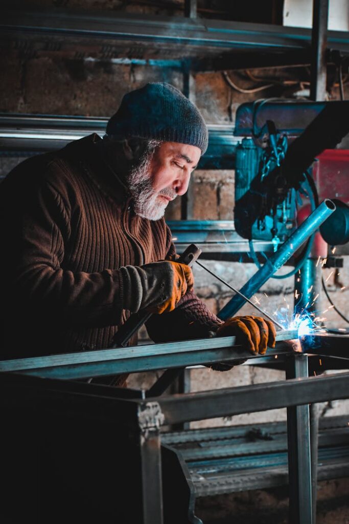 pexels-photo-15324248 A focused artisan welds metal with precision, creating sparks in a dimly lit workshop environment.